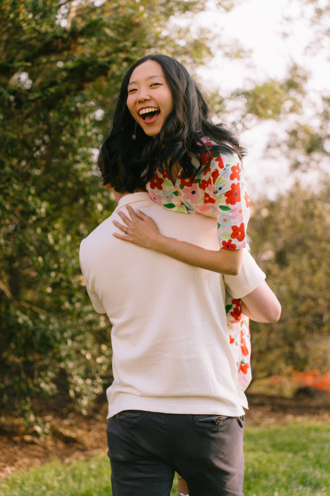 He lifts her over his shoulder as she laughs, in a floral dress