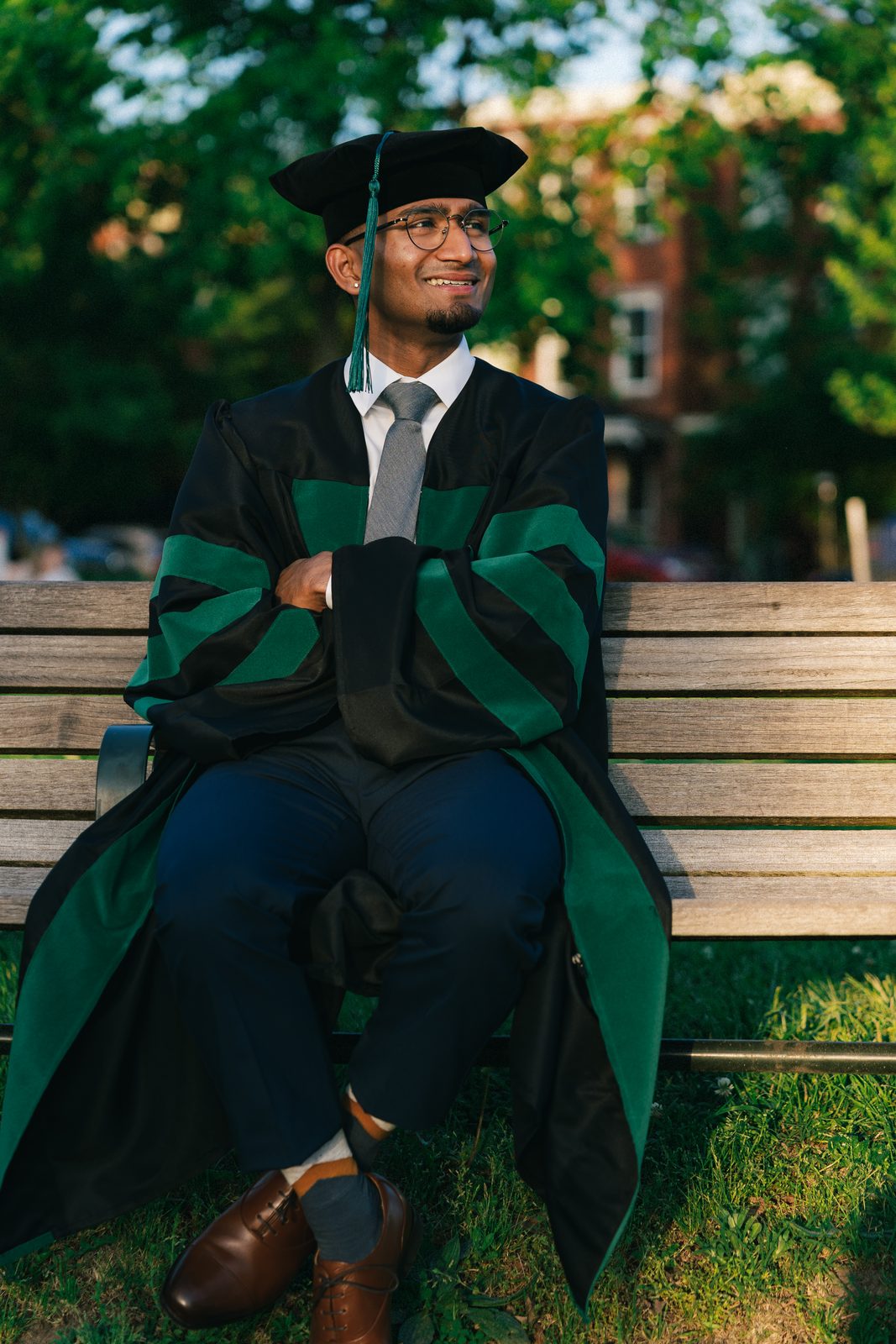 Graduate in cap and gown on a park bench in golden evening light