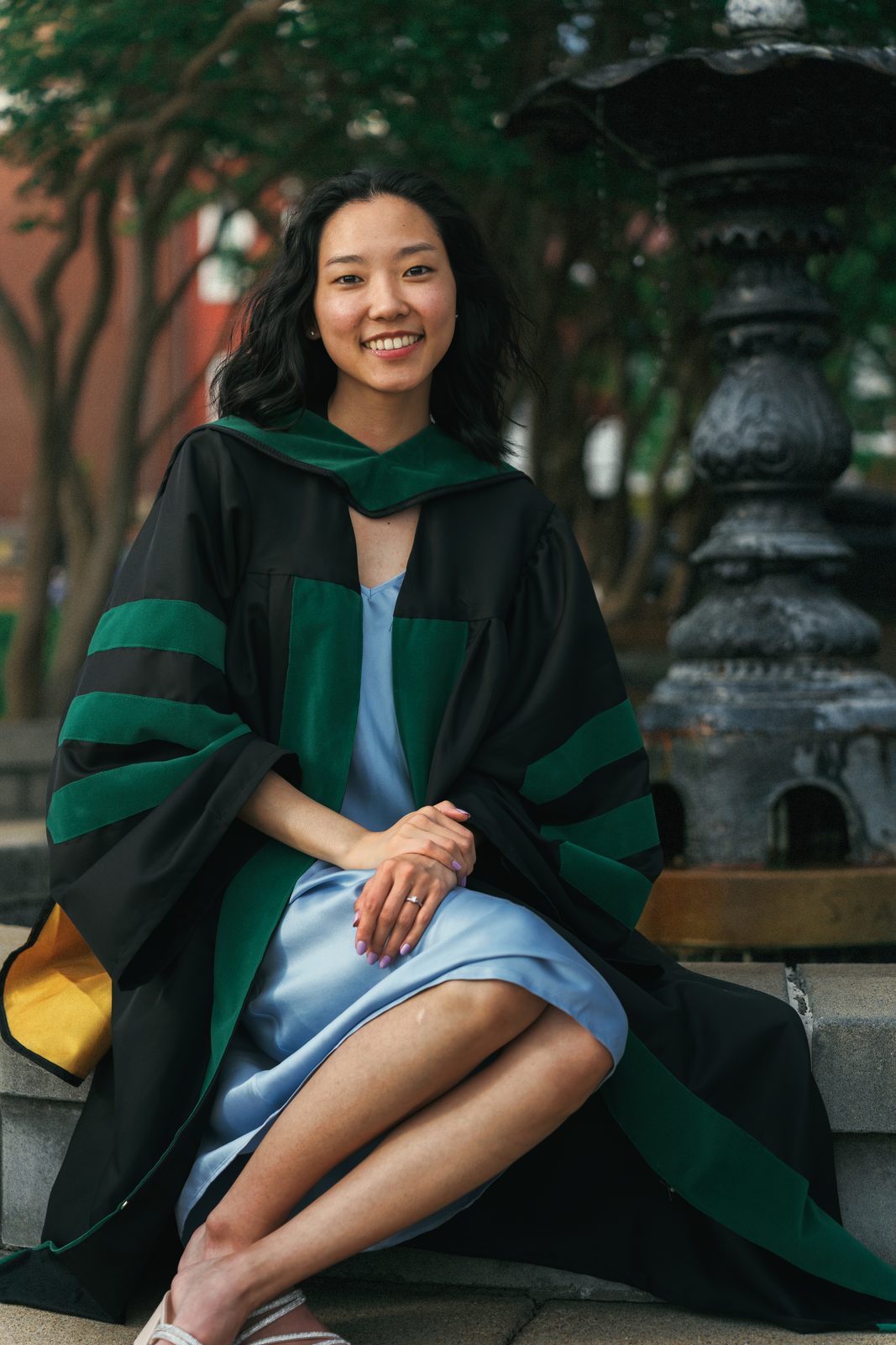 Graduate in a doctoral gown sitting by an iron fountain, smiling