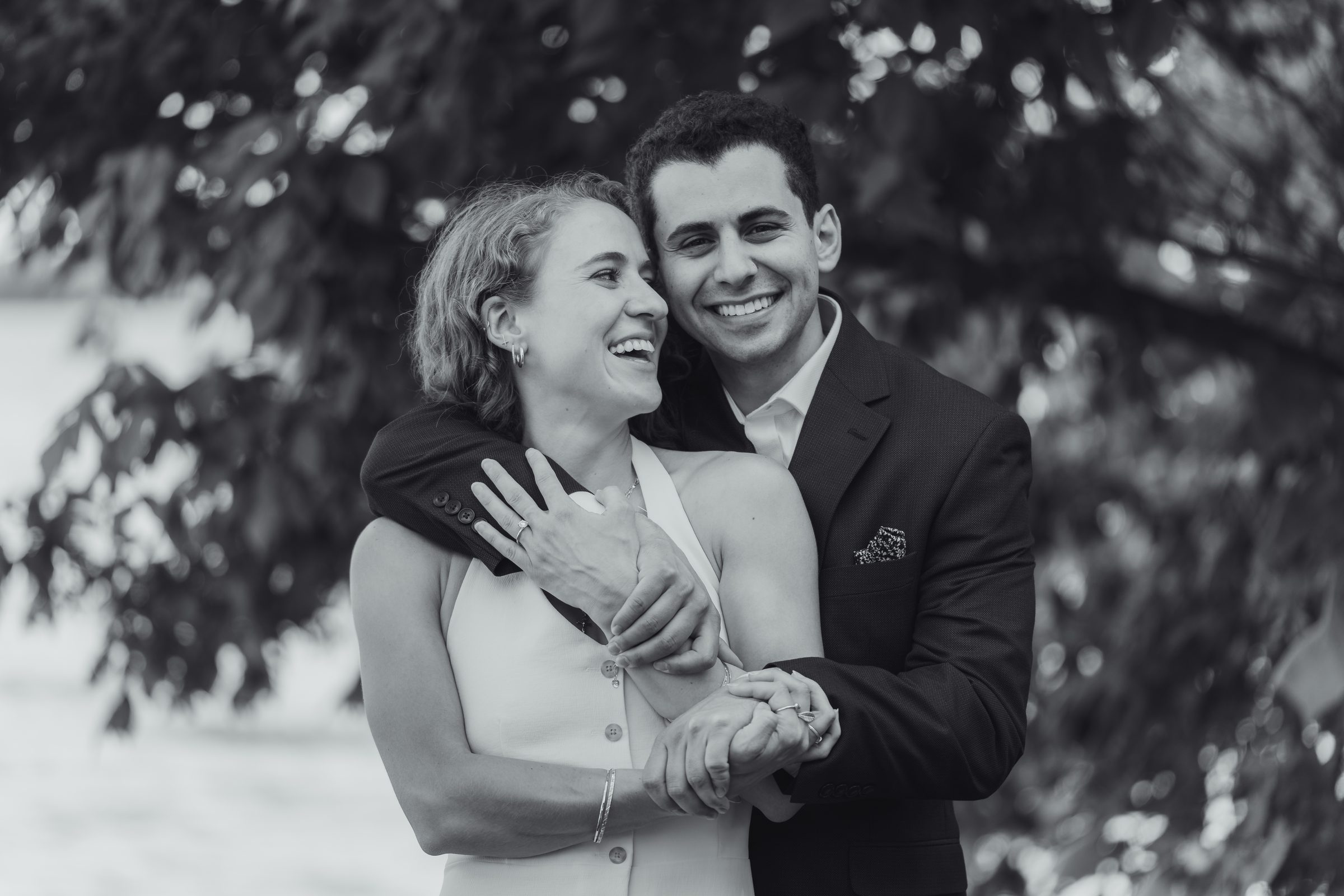 Black and white photo of a laughing couple embracing under a tree
