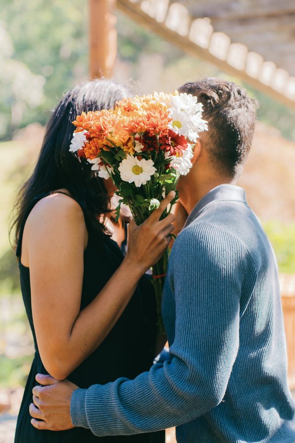 Couple kissing behind a bouquet of orange and white flowers