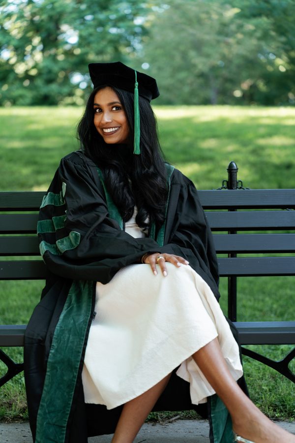 Graduate in cap and gown sitting on a park bench