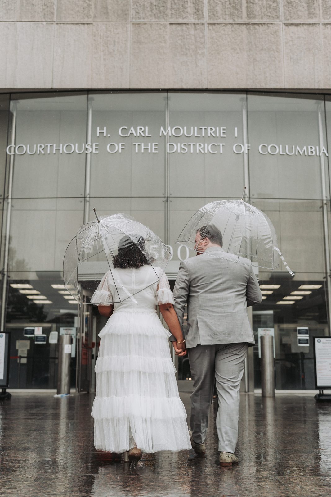 Couple walking hand in hand toward the courthouse under clear umbrellas