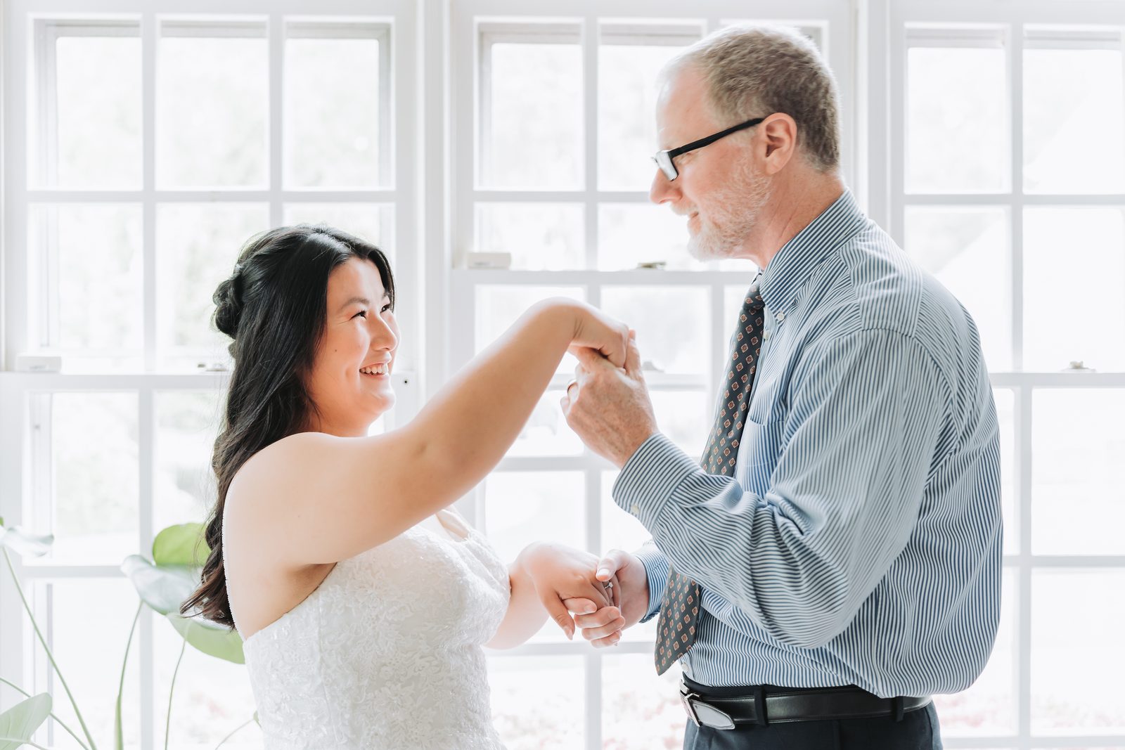 Bride twirling with her father during their dance by bright windows